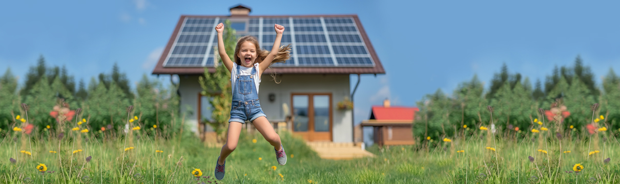 Hüpfendes Kind vor einem Haus mit Photovoltaikanlage auf dem Dach